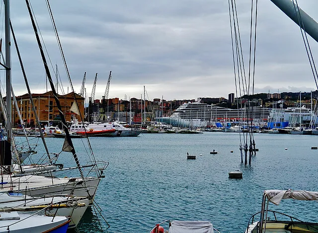 Sailboats moored in the Porto Antico of Genoa with a cruise ship and the hillside city behind